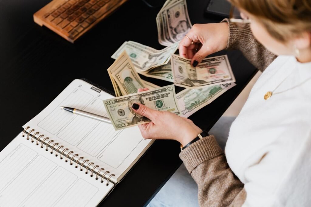 Mulher organizando finanças e contando dinheiro na mesa com caderno aberto para planejar o orçamento mensal